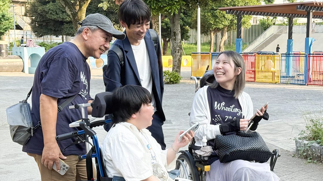 公園で車いすユーザーの女性とスタッフが笑顔で会話する様子