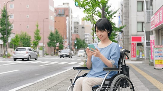 車いすユーザーの女性が路上でスマートフォンを操作する様子